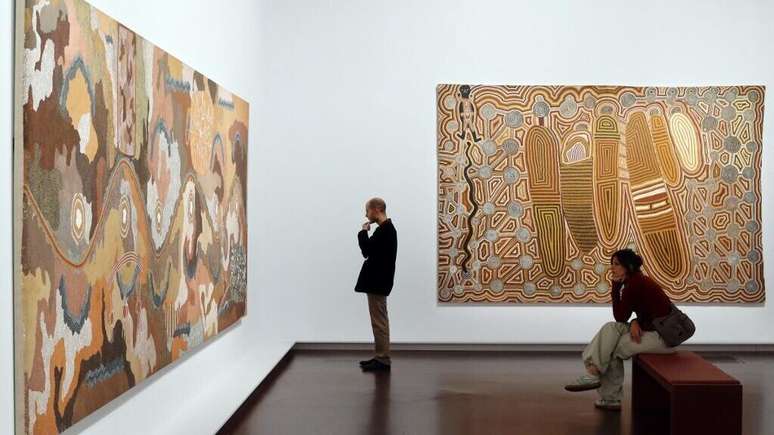 பழங்குடியின ஓவியர் கிளிஃபோர்ட் போஸம் ட்ஜபால்ட்ஜரி என்ற தலைப்பில் வரைந்த ஓவியத்தை ஒருவர் பார்க்கிறார் 