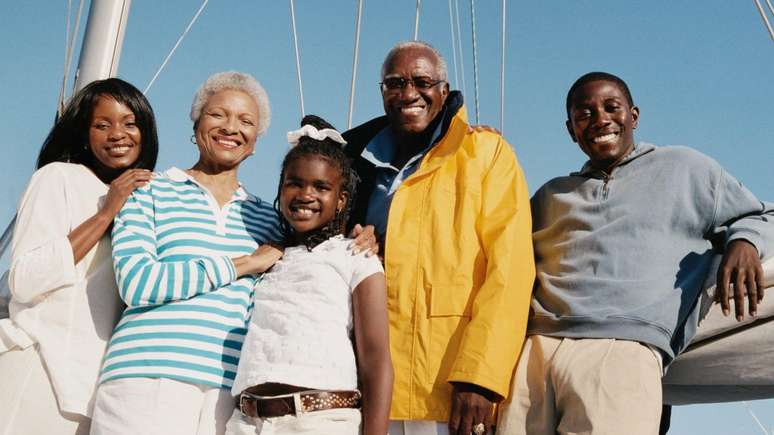 நான்கு தலைமுறைகளைக் கொண்ட ஒரு குடும்பம் புகைப்படத்திற்கு போஸ் கொடுக்கிறது. ஒரு பெண், 20 வயதில் ஒரு ஆணும், 40 வயதில் ஒரு பெண்ணும், 60 வயதில் ஒரு தம்பதியும் உள்ளனர். அவர்கள் ஒரு படகுக்கு முன்னால் இருக்கிறார்கள்.