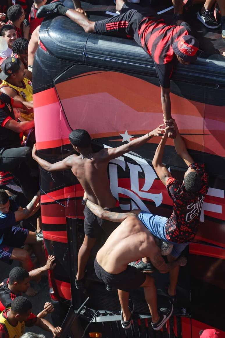 Torcedores se ajudam para subir no teto do &ocirc;nibus do Flamengo.