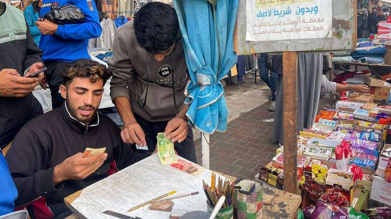 Baraa Abu Aoun repairs banknotes in a market in Gaza City