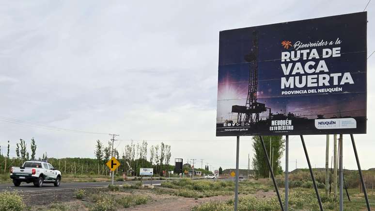 Estrada por onde passa uma caminhonete, com um cartaz dando as boas-vindas a Vaca Muerta