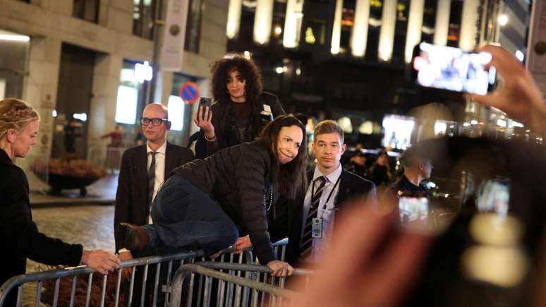 María Corina Machado salta as grades de segurança diante do Grand Hotel, em Oslo, para cumprimentar apoiadores que a aplaudem