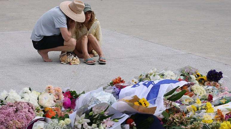 Two women console each other as they look at flowers laid in honor of the victims of Sunday's shooting (14/12/2025) at Bondi Beach in Sydney, Australia