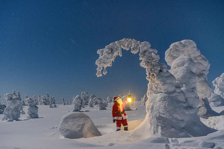 Papai Noel admirando escultura de gelo na regi&atilde;o da Lap&ocirc;nia, com a aurora boreal ao fundo