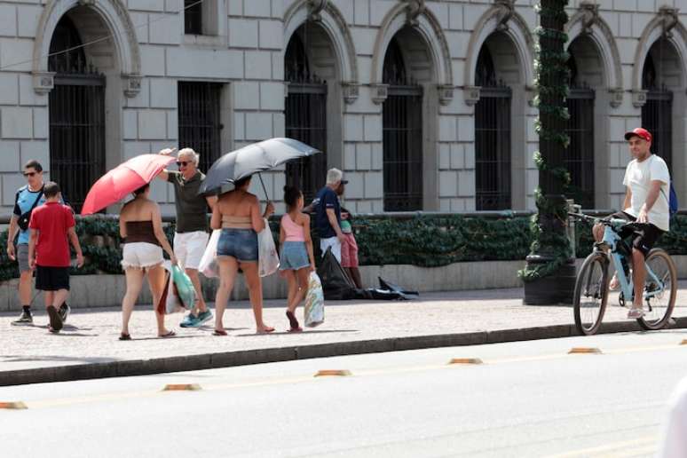 Pessoas na rua usam guarda-chuvas para se protegerem do sol e do calor intenso na cidade