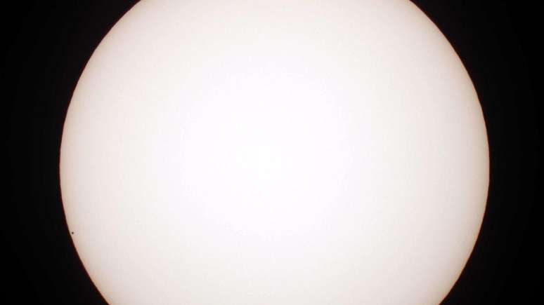 Merc&uacute;rio &eacute; realmente muito pequeno em compara&ccedil;&atilde;o com outros planetas. Aqui, ele aparece como um pontinho &agrave; esquerda, ao atravessar a frente do disco do Sol