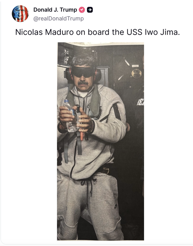 Um homem vestindo cal&ccedil;a e moletom, algemado e com os olhos vendados.