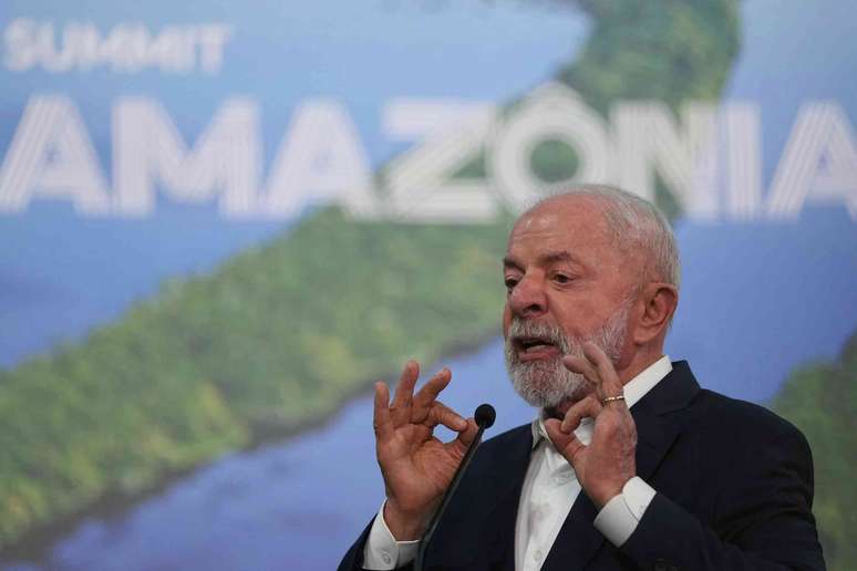 O presidente Lula gesticula com as m&atilde;os enquanto fala em frente a uma foto da Amaz&ocirc;nia.
