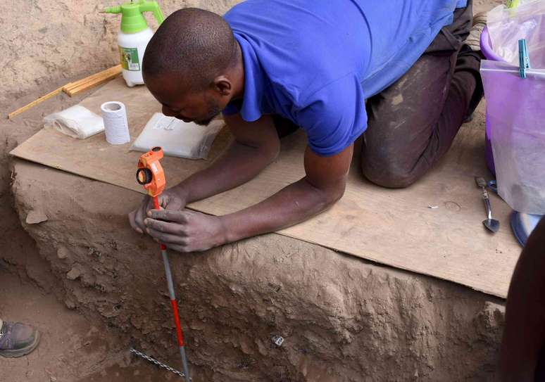 homem ajoelhado em uma t&aacute;bua mede a &aacute;rea escavada