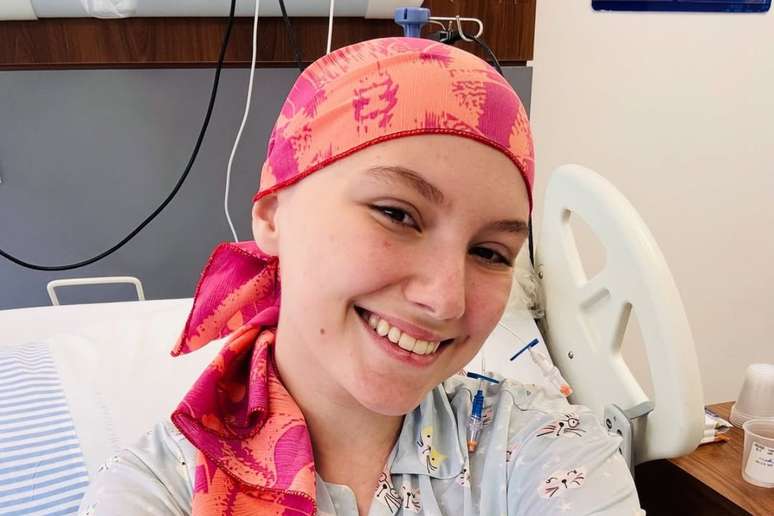 இசபெல் வெலோசோ ஒரு புகைப்படத்திற்காக புன்னகைக்கிறார், பின்னணியில் நீங்கள் ஒரு மருத்துவமனை படுக்கையைக் காணலாம்