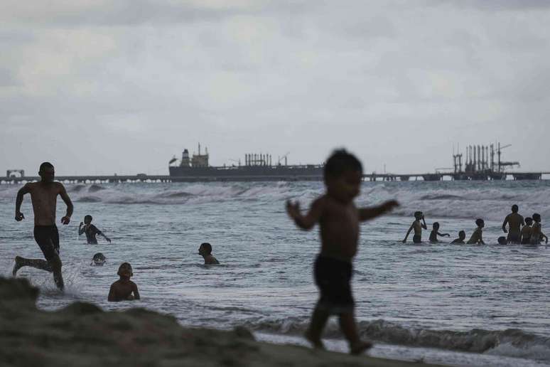 Pessoas passam o tempo em uma praia com um petroleiro nas proximidades.