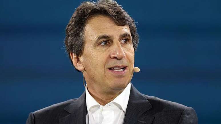 O empres&aacute;rio Marc Rowan olhando para a direita com um microfone preso ao rosto, vestido com um terno preto e sentado em frente a um fundo azul.