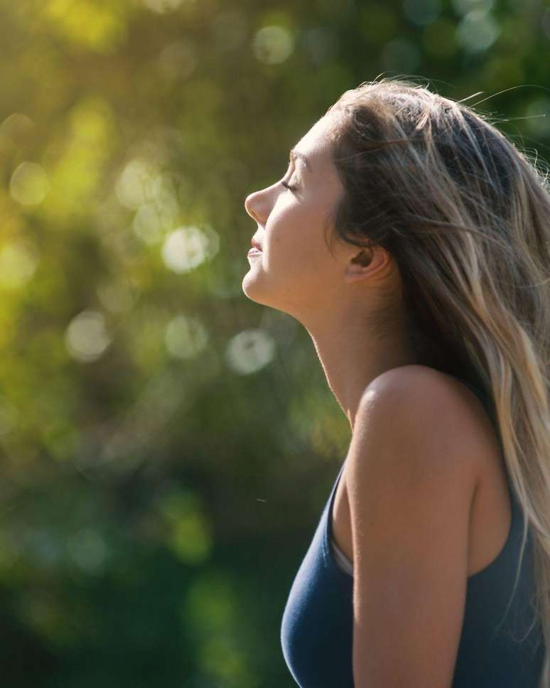 Mulher branca loira olhando para o c&eacute;u com o sol no rosto.