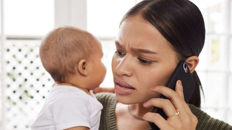Mulher segurando um beb&ecirc; no colo, falando no telefone celular.