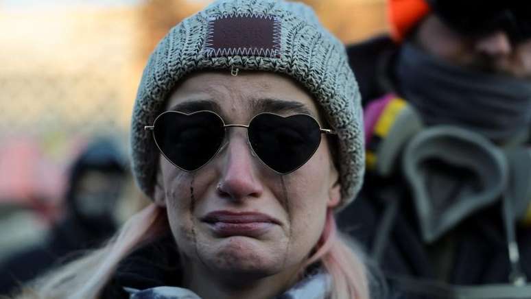 Uma mulher chora enquanto as pessoas se re&uacute;nem em torno de um memorial improvisado perto do local onde Alex Pretti foi baleado.