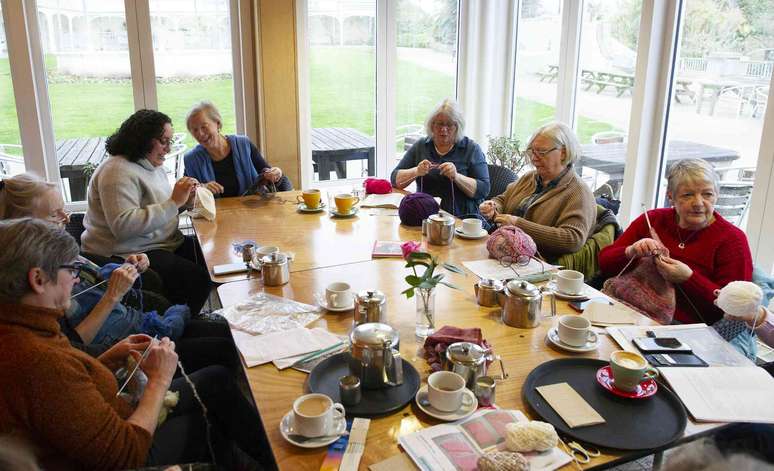 Mulheres idosas tricotando juntas e socializando em um espa&ccedil;o comunit&aacute;rio.