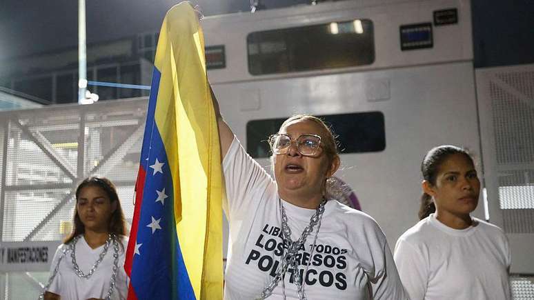Uma mulher segurando a bandeira da Venezuela e usando uma blusa escrito "Liberta todos os presos pol&iacute;ticos"
