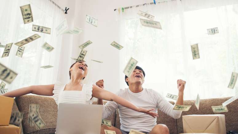 casal recebendo chuva de dinheiro sentado no sof&aacute; da sala