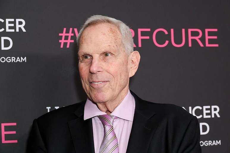 Steve Tisch usa um terno preto, uma camisa rosa e uma grava rosa. 