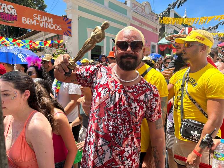 Vin&iacute;cius Matos se fantasia de Dona Sebastiana, personagem de 'O Agente Secreto', segurando o Oscar no bloco Pitombeiras