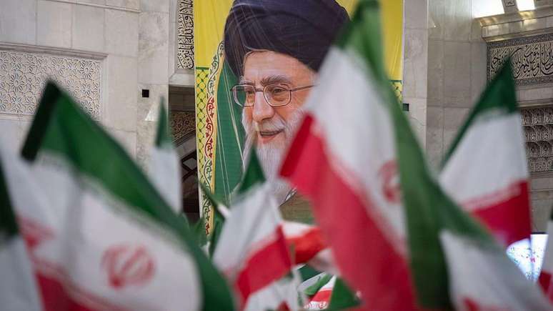 Bandeiras iranianas com um cartaz retratando o l&iacute;der do pa&iacute;s, Ali Khamenei, ao fundo