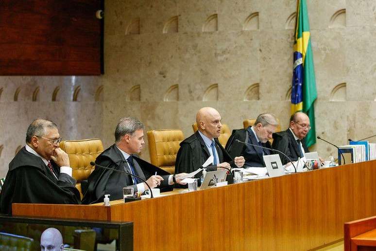 Dino, Mendon&ccedil;a, Moraes, Toffoli e Gilmar Mendes sentados lado a lado no plen&aacute;rio do STF, ventindo terno e suas togas de ministro; Moraes fala ao microfone enquanto os demais escutam