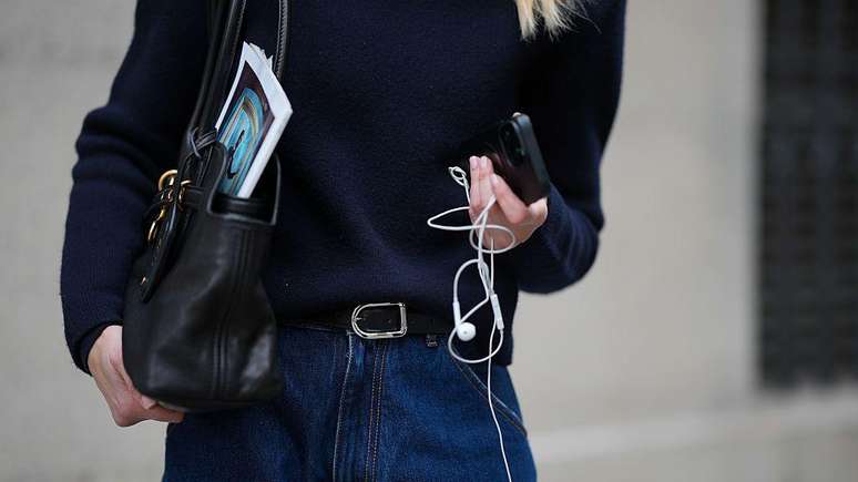 Mulher segurando fones de ouvido com fio e um celular. 