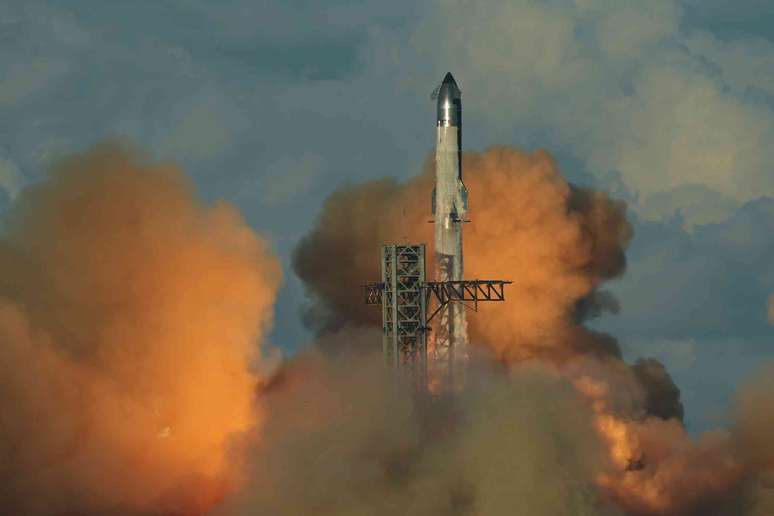 Um grande foguete sendo lan&ccedil;ado ao c&eacute;u, cercado por nuvens de fuma&ccedil;a.