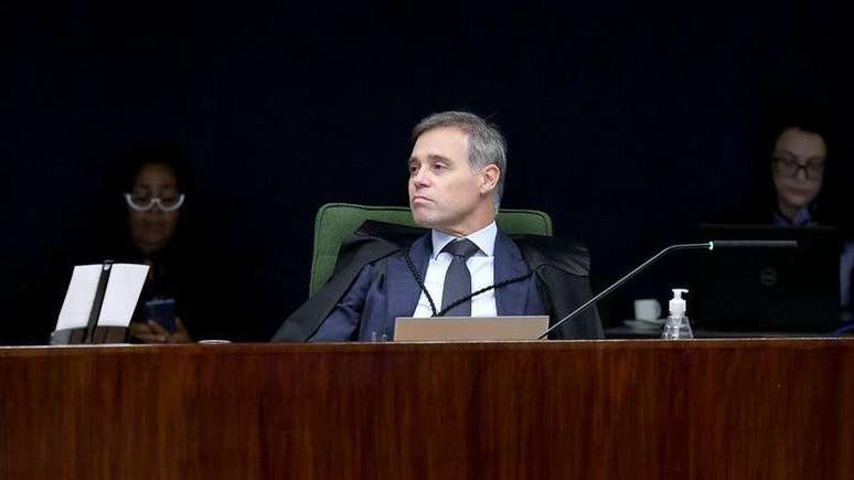Andr&eacute; Mendon&ccedil;a, sentado, durante julgamento no Plen&aacute;rio da Primeira Turma do STF. Atr&aacute;s dele, em segundo plano, duas pessoas acompanham sentadas, com olhar para baixo. 