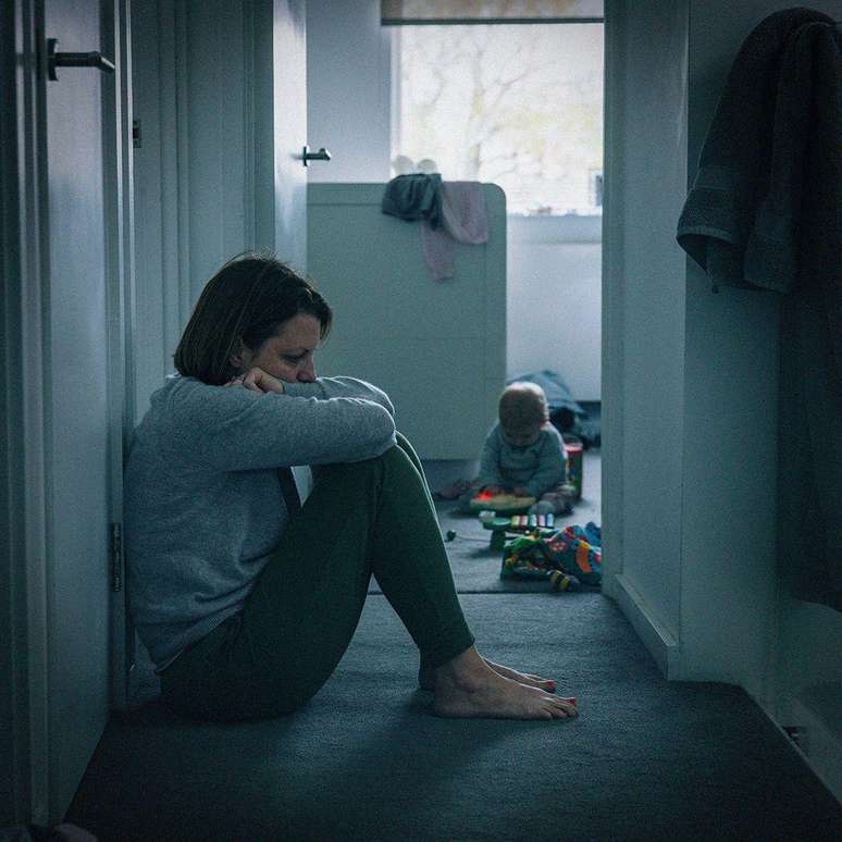 M&atilde;e sentada no ch&atilde;o, no lado de fora do quarto da crian&ccedil;a