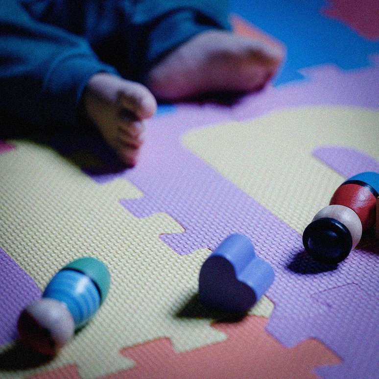 Crian&ccedil;a sobre um tapete infantil, com brinquedos de madeira