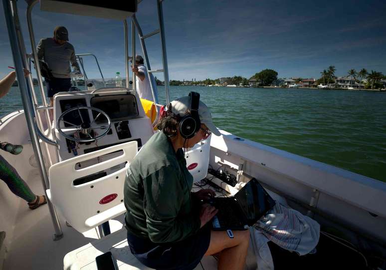 Uma mulher em um barco usando fones de ouvido e olhando para um laptop