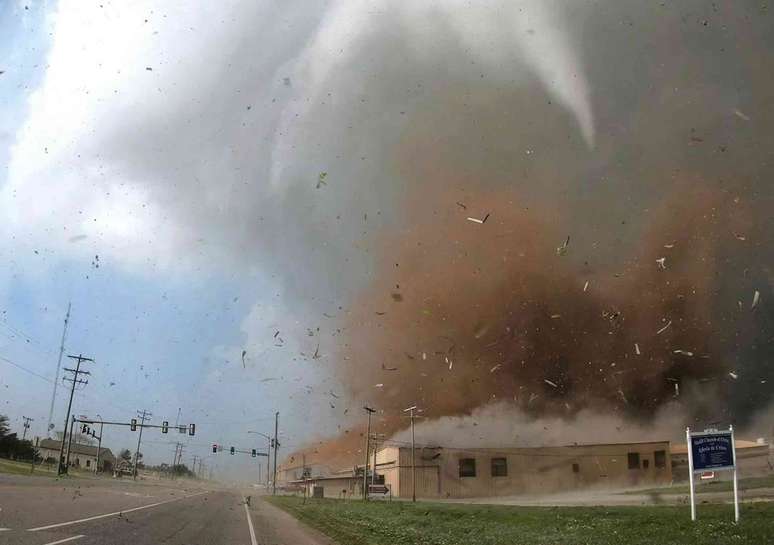 Um tornado destr&oacute;i um pr&eacute;dio, lan&ccedil;ando uma nuvem de detritos em alta velocidade no ar.