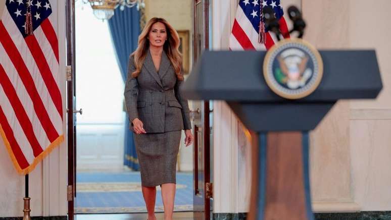 Melania Trump veste um terno com saia e caminha em dire&ccedil;&atilde;o a um p&oacute;dio com o selo presidencial na Casa Branca