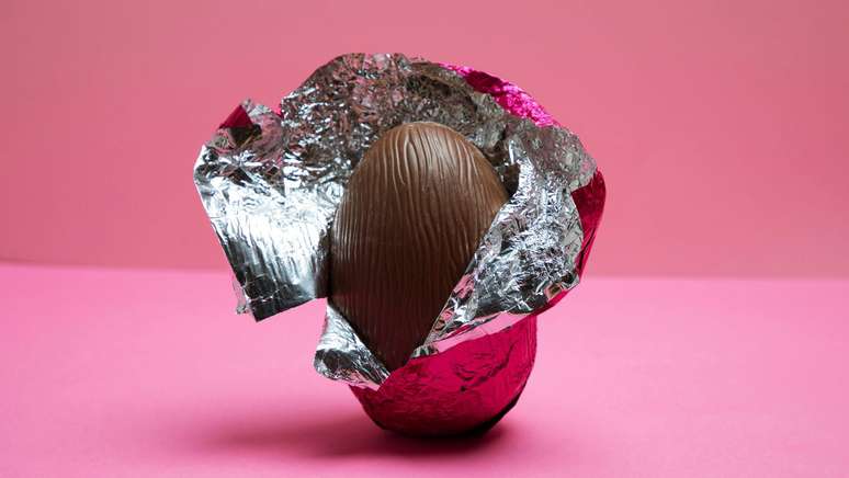 Um ovo de p&aacute;scoa com embalagem aberta em fundo rosa