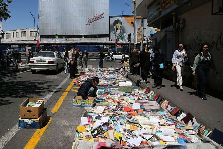 Um livreiro disp&otilde;e centenas de livros &agrave; beira de uma estrada em Teer&atilde; enquanto as pessoas passam.