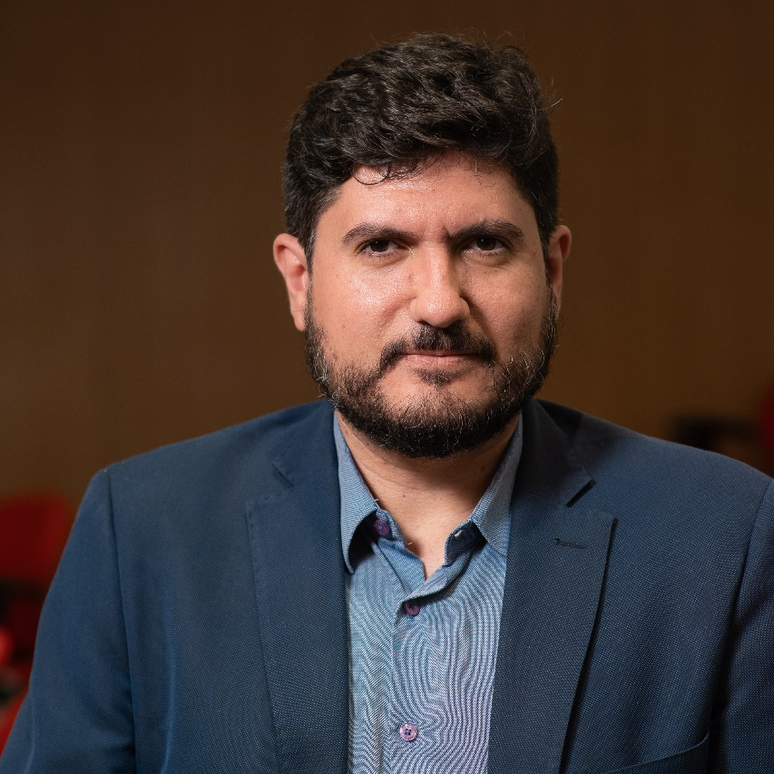 Guilherme Casar&otilde;es em retrato com semblante s&eacute;rio, camisa de bot&atilde;o e blazer azuis. 