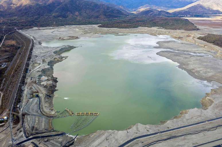 Uma grande lagoa de reten&ccedil;&atilde;o com bordas irregulares, estradas ao longo de suas margens e montanhas ao fundo.