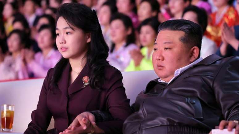 Kim Ju Ae e Kim Jong Un deram a m&atilde;os enquanto assistiam a uma apresenta&ccedil;&atilde;o em comemora&ccedil;&atilde;o ao Dia Internacional da Mulher, no Gin&aacute;sio Ryugyong Chung Ju-yung, em Pyongyang, em 8 de mar&ccedil;o de 2026