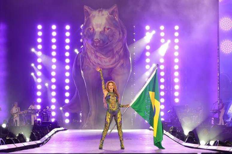 Shakira no palco em Copacabana, segurando uma bandeira do Brasil com uma est&aacute;tua de um lobo gigante ao fundo