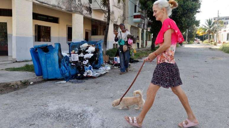 Em Havana, pessoas caminham ao lado de uma grande lixeira incendiada na noite anterior em protesto contra os prolongados apag&otilde;es