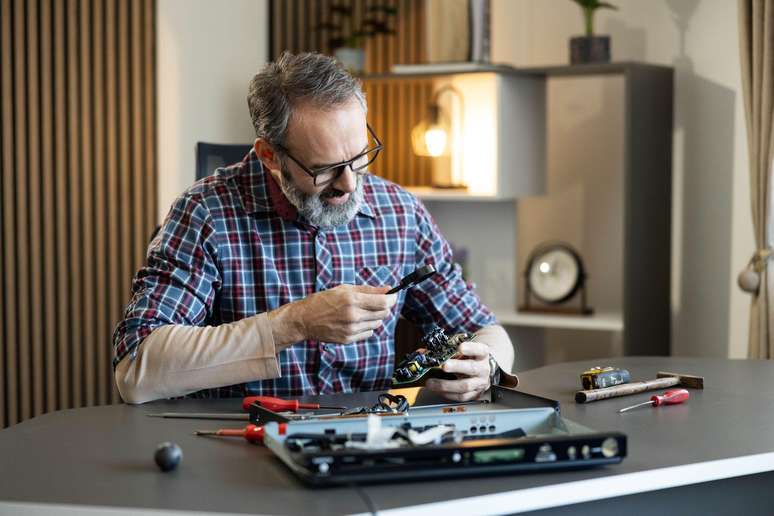 Um homem consertando um cart&atilde;o de mem&oacute;ria de um computador. Ele segura uma lupa na m&atilde;o.
