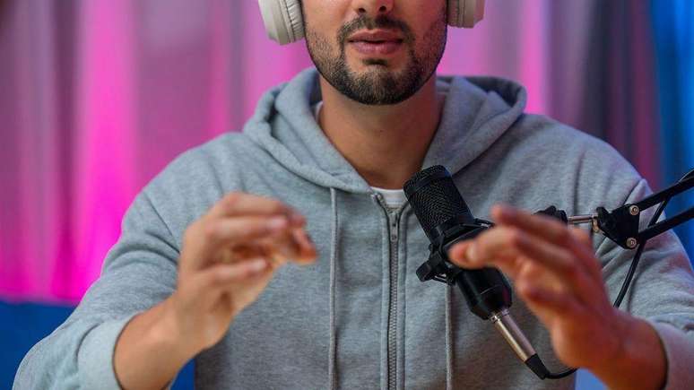 Um jovem de moletom cinza falando ao microfone em um est&uacute;dio de podcast profissional.