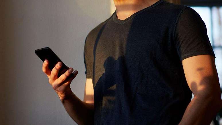 Um homem usando uma camisa preta e com o celular na m&atilde;o