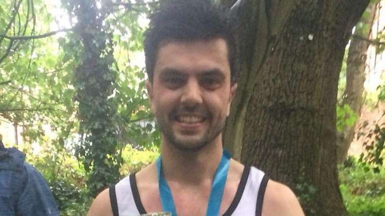 Will veste uma camiseta esportiva e usa uma faixa azul ao redor do pesco&ccedil;o, que parece ser uma medalha. Ele sorri para a c&acirc;mera e est&aacute; em um ambiente cheio de &aacute;rvores.