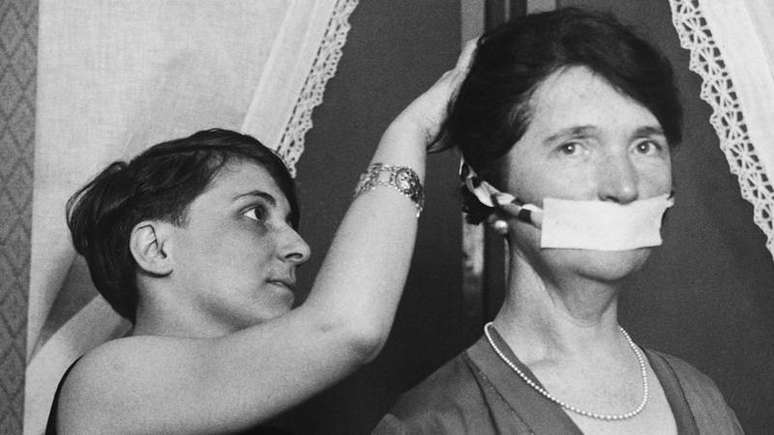 'Nenhuma mulher pode se considerar livre se n&atilde;o controlar seu pr&oacute;prio corpo': Margaret Sanger (&agrave; direita) usando uma m&aacute;scara em protesto por ter sido impedida de falar sobre controle de natalidade em Boston, em 1929