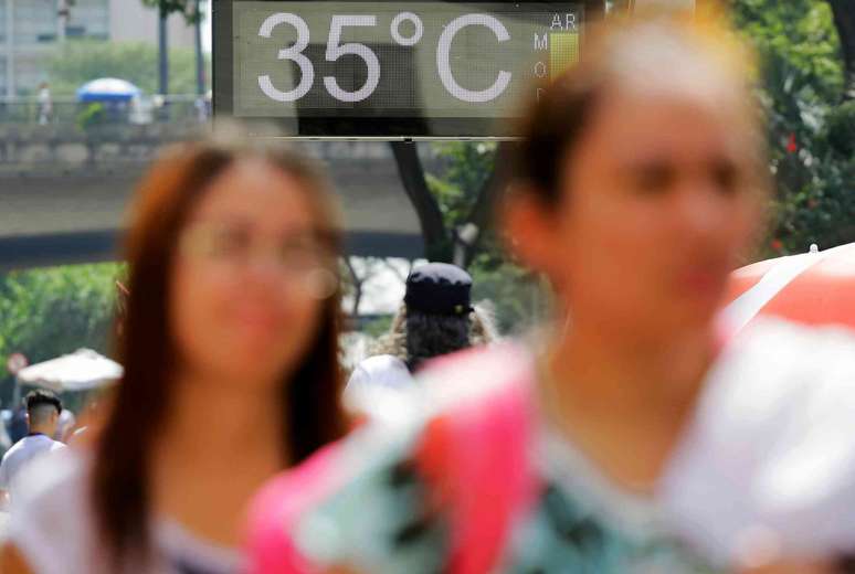 duas mulheres caminhando pela rua, placa de tr&acirc;nsito ao fundo indica 35 graus, sinalizando clima quente