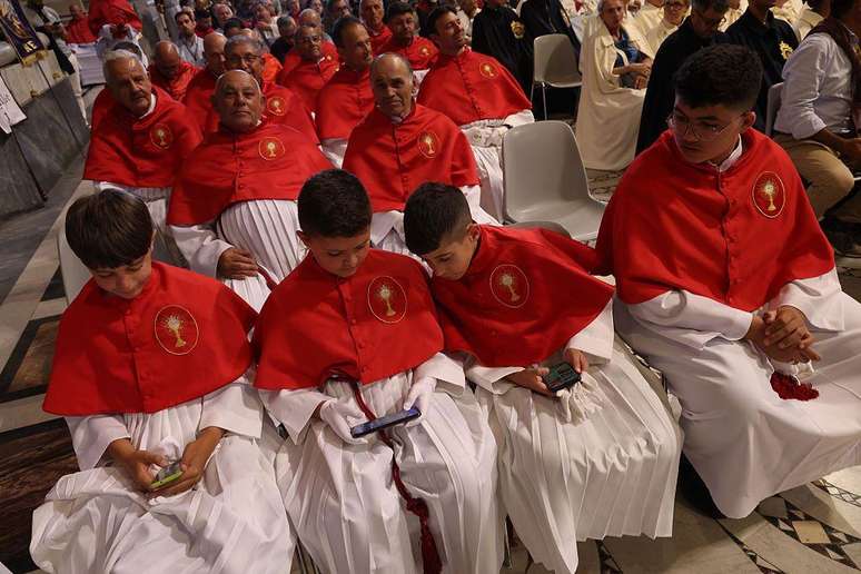 Membros de uma confraria cat&oacute;lica maltesa, incluindo crian&ccedil;as que est&atilde;o olhando para seus smartphones, participam do evento de boas-vindas na Bas&iacute;lica de S&atilde;o Jo&atilde;o de Latr&atilde;o durante o Jubileu das Confrarias em 16 de maio de 2025 em Roma, It&aacute;lia.