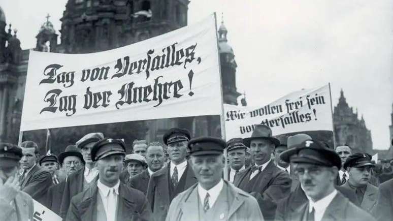 Apoiadores nazistas marcham em Berlim em 1938 durante uma manifesta&ccedil;&atilde;o contra o Tratado de Versalhes, que encerrou a Primeira Guerra Mundial e imp&ocirc;s duras restri&ccedil;&otilde;es e repara&ccedil;&otilde;es &agrave; Alemanha