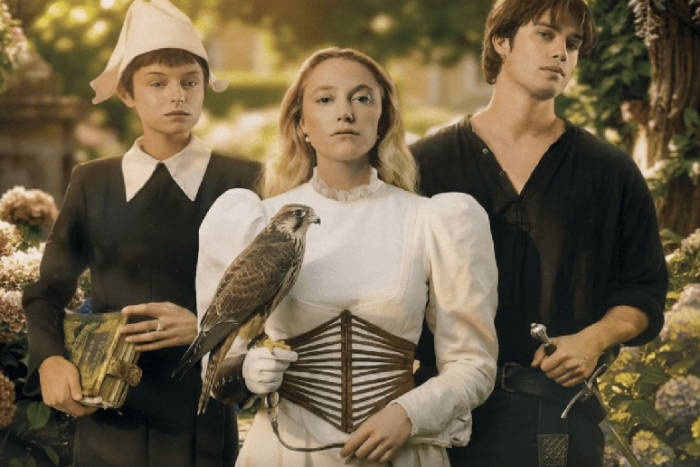 Tr&ecirc;s personagens em trajes de &eacute;poca posando em um jardim, enquanto uma mulher segura um falc&atilde;o sobre a m&atilde;o enluvada